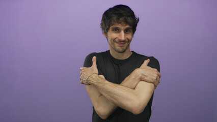 Young man wearing black shirt hugging his arms across chest with soft smile in purple studio;...