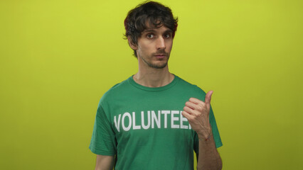 Man wearing a branded green volunteer t shirt and raised thumb points to side in studio setting;...