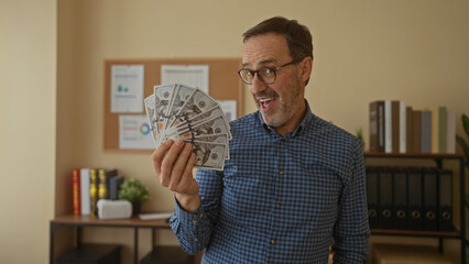 Man holding cash indoors in an office setting with a joyful expression, surrounded by books and...