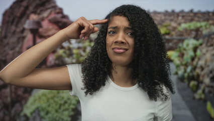 African american woman wearing white tshirt points finger to head in green park; uncertainty...