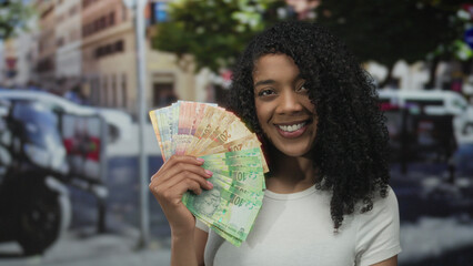 Woman holding a colorful fan of rand banknotes amid busy cars in a bustling city street; joy...