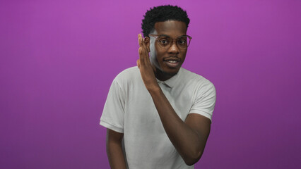 Man makes flat palm gesture at his chin wearing a white polo shirt in a studio with a purple wall;...