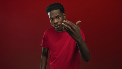 Young black man beckons hand forward in studio environment, looking directly forward and extending...