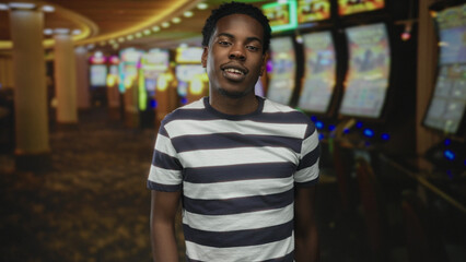 Fototapeta premium Young man does finger salute to head while standing by slot machine under neon lights in casino; excitement.