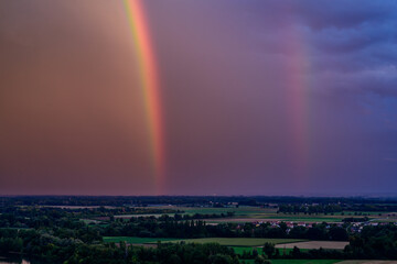 Bunter Regenbogen über den grünen Feldern während eines stürmischen Himmels