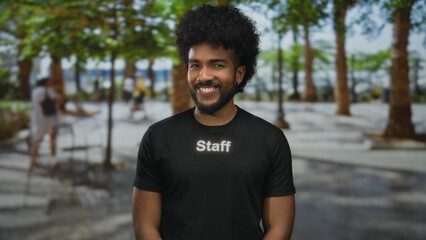 Man in staff uniform smiling outdoors city street surrounded by greenery trees vibrant atmosphere...