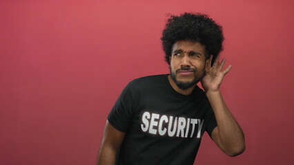Man in security uniform poses against red wall listening intently isolated in studio setting.