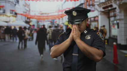 Policeman presses his hands together in prayer on a crowded city street with blurred pedestrians...