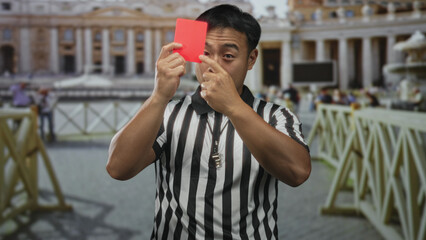 Man in referee uniform holds red card while blowing whistle and pointing finger in building;...