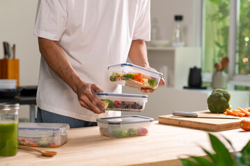 Man preparing healthy homemade meal prep in food container with fresh food at home.