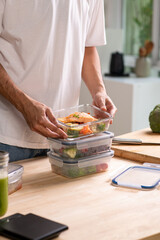 Man preparing healthy homemade meal prep in food container with fresh food at home.