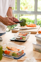 Person using smartphone app for calorie counting and photo sharing above homemade weight loss meal prep.