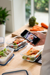Man taking photo with phone while preparing healthy homemade meal prep with fresh food at home.