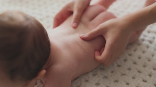 Mother massaging baby back and bottom with gentle caring hands