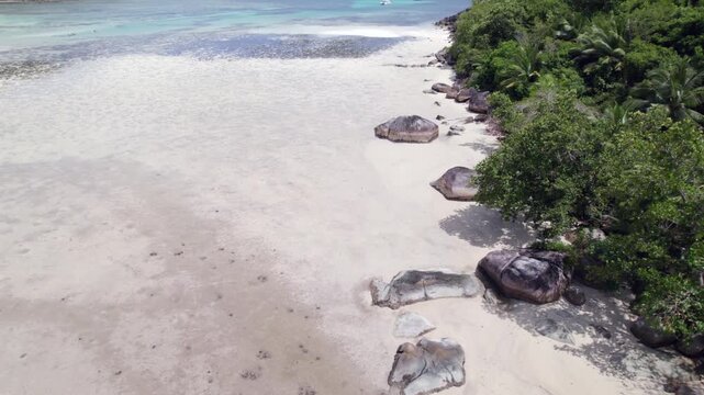 Drone footage of cap ternay beach, near granite stone and trees at low tide, Mahe, Seychelles 30fps