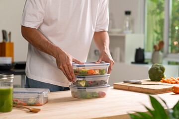 Man preparing healthy homemade meal prep in food container with fresh food at home.