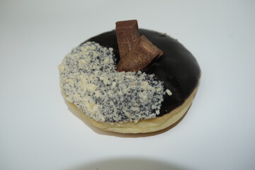 Close-up of a sweet donut covered in chocolate glaze, sprinkled with crumbs, and topped with two chocolate candy pieces.
