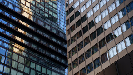 Fototapeta premium Close-up of two modern high-rise buildings with glass and metal facades reflecting each other in an urban setting