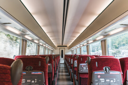 Inside view of modern japanese high speed train carriage with comfortable red seats, large windows and bright ceiling light during travel - Powered by Adobe