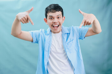 Cheerful Young Man Pointing at the Camera with a Bright Smile Against a Light Blue Background