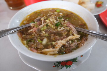 Bowl of sroto, a traditional Indonesian beef soup with bean sprouts, herbs, and savory broth, served hot with rice cakes on the side.
