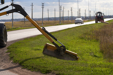 Maintenance of a rural road. Two tractors mow the grass on the side of the road.