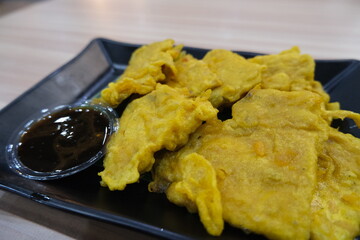Traditional Indonesian dish called mendoan, made from thinly sliced tempeh coated in spiced batter and deep-fried, served with sweet soy sauce.
