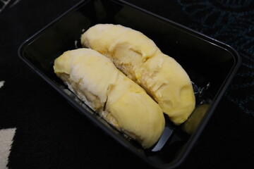 Two pieces of frozen durian pulp with creamy yellow flesh placed in a black plastic tray, ready to be served or stored.
