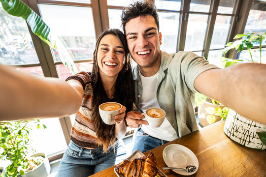 Happy couple enjoying breakfast drinking coffee at bar cafeteria - Life style concept with guy and girl in love having date moment sitting at restaurant in the city centre