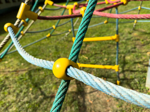 Closeup of colorful rope climbing net detail with yellow connector on playground structure in outdoor park for children and kindergarten play.