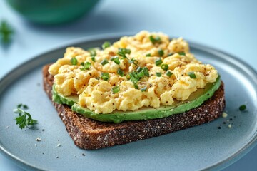Close-up of a slice of seeded whole grain bread topped with creamy mashed avocado, scrambled eggs, chopped green onions, and black pepper on a light blue plate