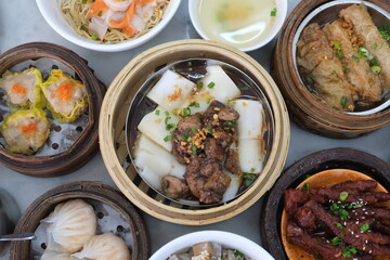 Top view of various traditional Chinese dim sum dishes served in bamboo steamers and bowls, including dumplings, noodles, and meats.
