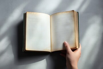 Hand holding an open old book with blank, yellowed pages illuminated by soft natural light