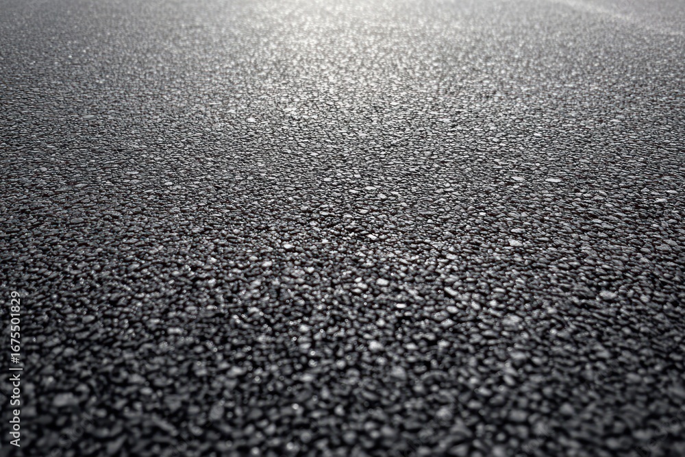 Poster close-up of textured asphalt road surface with visible small stones and rough granules reflecting li