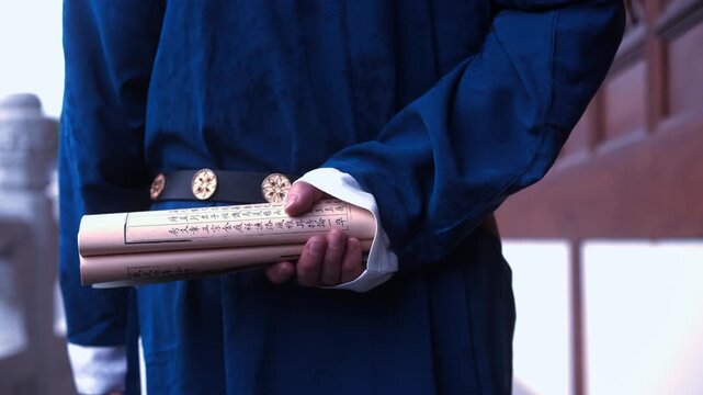 A person in traditional blue ancient Chinese attire holding a rolled scroll in close-up view