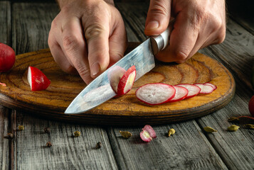 A pair of hands skillfully slices vibrant radishes with a sharp knife on a rustic wooden cutting...