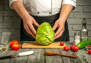A chef holds a large green cabbage while surrounded by fresh vegetables like tomatoes, radishes,...