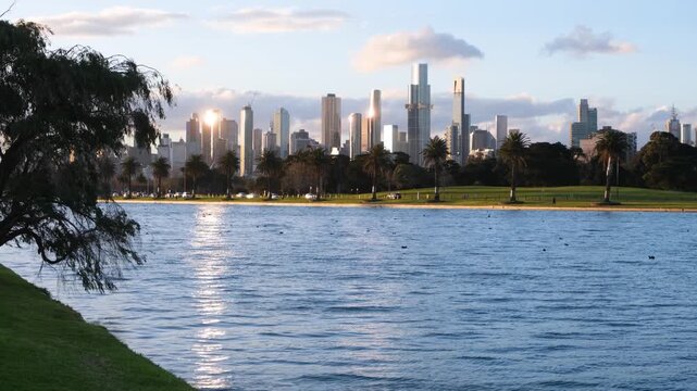 Scenic view of Melbourne city skyline at sunset, with Albert Park Lake in the foreground, and flowing traffic at the waterfront. Metropolitan lifestyle in Victoria, Australia.
