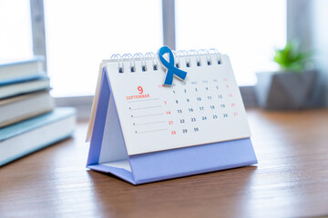 A calendar is open to the month of September, with a blue awareness ribbon clipped to the top of...