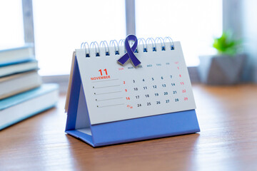 A calendar is open to the month of November, and a purple awareness ribbon is clipped to the top of...