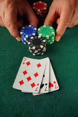 Two hands place poker chips on a green table, showcasing a pair of playing cards with diamonds and...