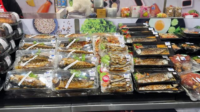 Close view of assorted cooked fish packaged in plastic trays at a retail grocery counter.