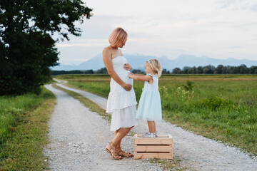 Pregnant mother and daughter in nature. Little girl hugs mom's belly. Family and Pregnancy.