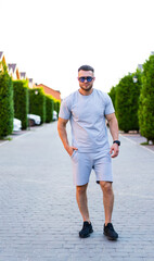 Obraz premium Man in casual wear on sunny street. A man in a gray outfit strolls down a residential street lined with neatly trimmed trees under bright blue skies.
