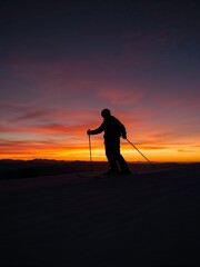 Dramatic Sunset Skiing Silhouette: Solitary Skier on a Mountain Slope Amidst Fiery Winter Sky and Alpine Peaks