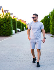Man strolls summer street. A man dressed in a gray outfit strolls along a tree-lined residential...
