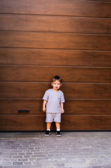 Young boy poses near wooden garage door. A young boy stands confidently by a wooden garage door,...