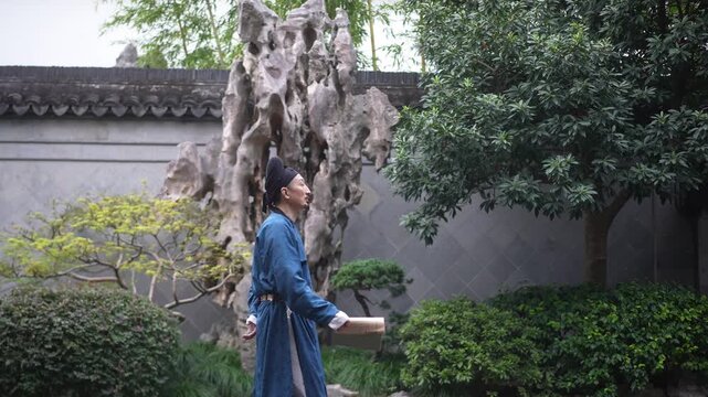 A man in blue traditional attire walks through a classical Chinese garden holding a scroll beside an ancient tree