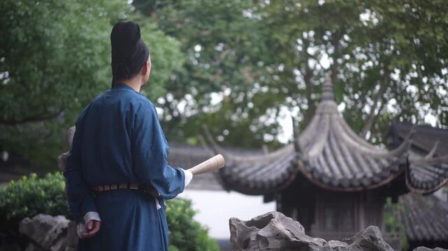 A man in traditional Chinese attire stands with his back to the camera holding a scroll in front of a pavilion in a Jiangnan-style classical garden