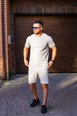 Man in casual summer style. A man in a gray t-shirt and shorts stands outside a garage, enjoying...